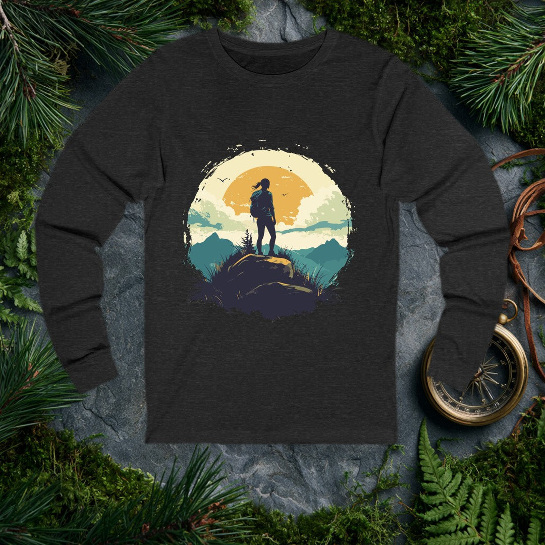 A lone hiker with a ponytail and pack stands on a boulder at golden hour, mountains layered blue behind her and two birds cutting across a wide amber sun. For…