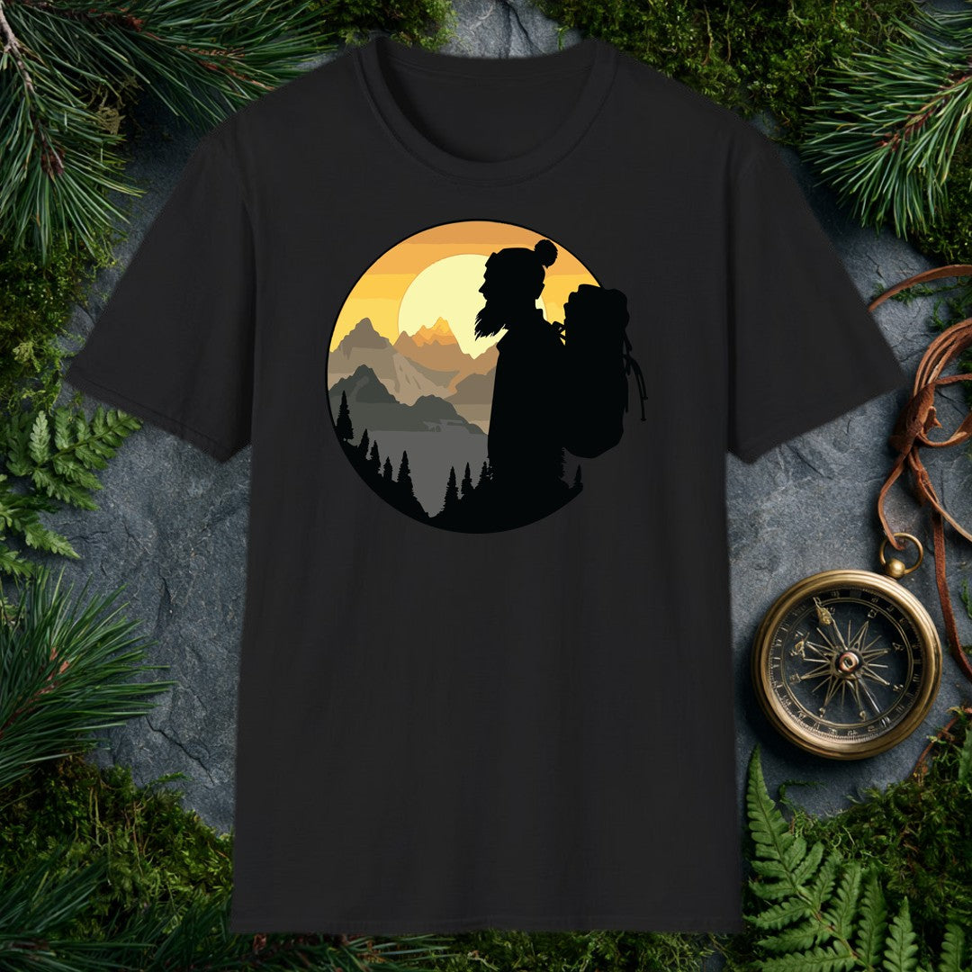 A silhouetted hiker — wool pom hat, long hair, full pack on her back — faces a layered mountain range as the sun crests behind jagged peaks above a pine-lined…