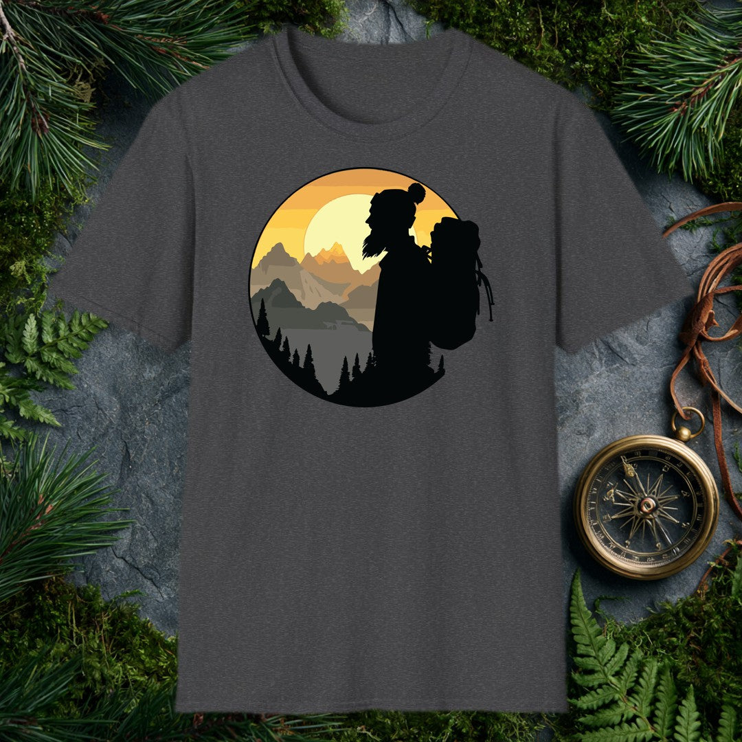 A silhouetted hiker — wool pom hat, long hair, full pack on her back — faces a layered mountain range as the sun crests behind jagged peaks above a pine-lined…