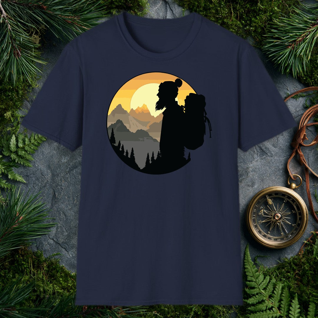 A silhouetted hiker — wool pom hat, long hair, full pack on her back — faces a layered mountain range as the sun crests behind jagged peaks above a pine-lined…