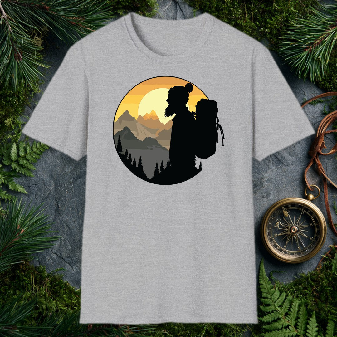 A silhouetted hiker — wool pom hat, long hair, full pack on her back — faces a layered mountain range as the sun crests behind jagged peaks above a pine-lined…