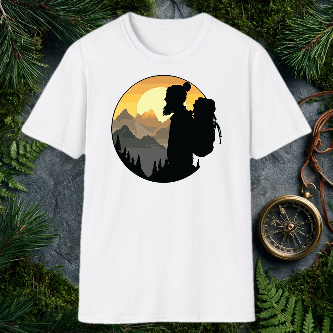 A silhouetted hiker — wool pom hat, long hair, full pack on her back — faces a layered mountain range as the sun crests behind jagged peaks above a pine-lined…
